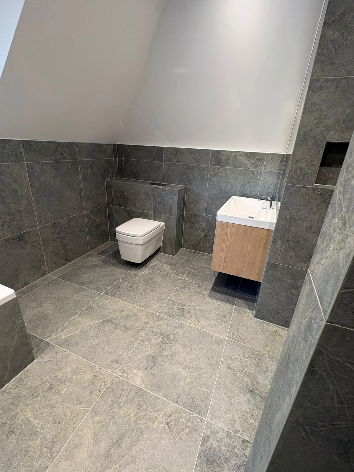 After: the finished grey stone loft bathroom with wall-hung toilet and oak vanity